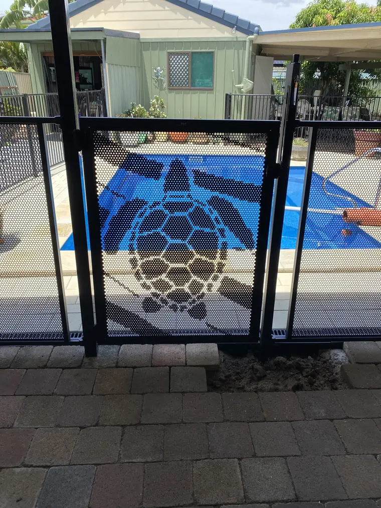 A black pool gate with a large sea turtle cut into it, the blue of the pool showing through the turtle