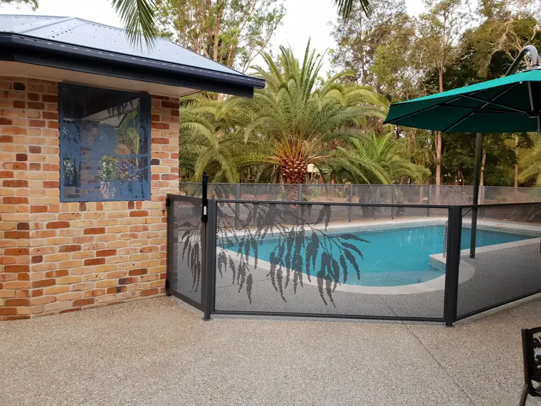 An Ironstone pool gate cut with gum leaves beside a curved pool, with a brick wall and palm trees behind