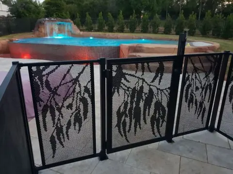 A black Gum design gate between Gum panels, beside a pool and spa lit up at dusk