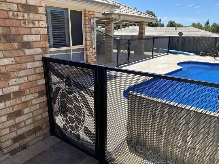 A turtle gate in a black PurePerf fence against a brick wall, beside a curved pool
