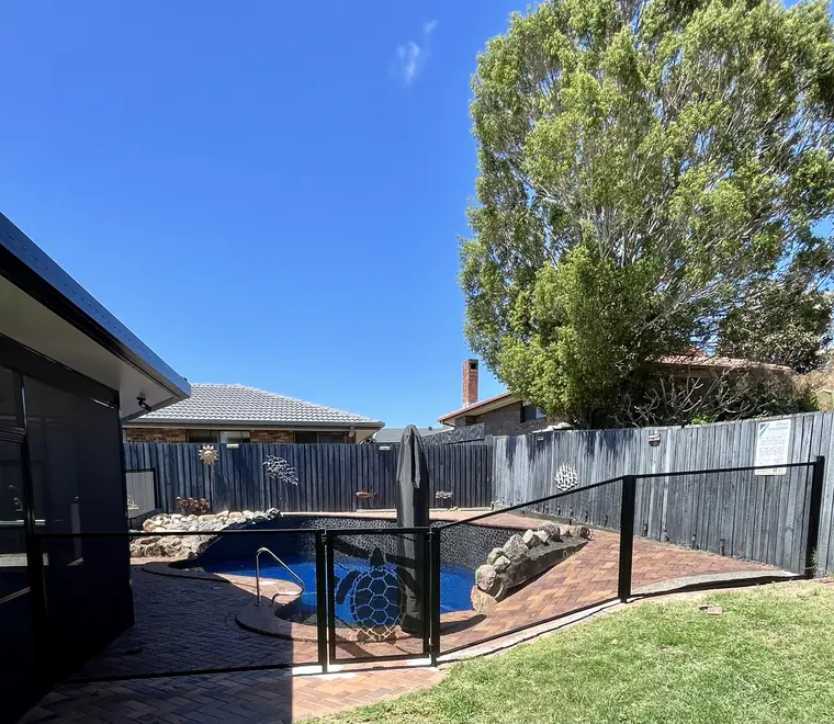 A black PurePerf pool fence curving around a pool and lawn, with a turtle cut into the gate