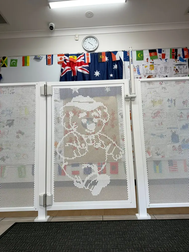 A white gate with a koala cut into it, inside a childcare centre with an Australian flag on the wall