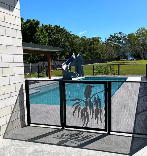 A black pool gate with a kookaburra on a gum branch, beside a pool with a slide