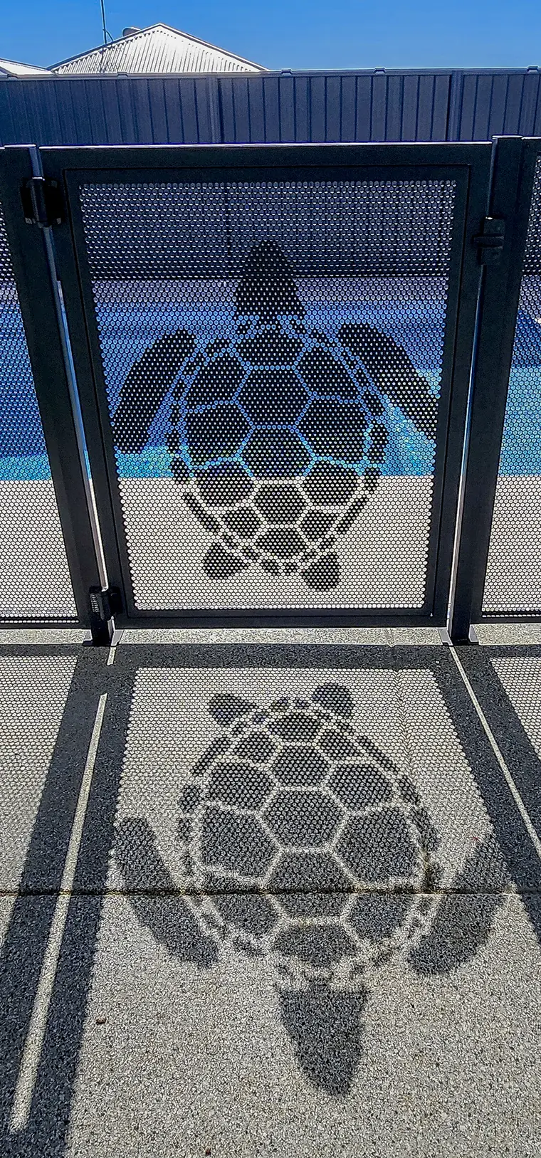A turtle gate seen straight on, with the turtle repeated in its shadow on the paving