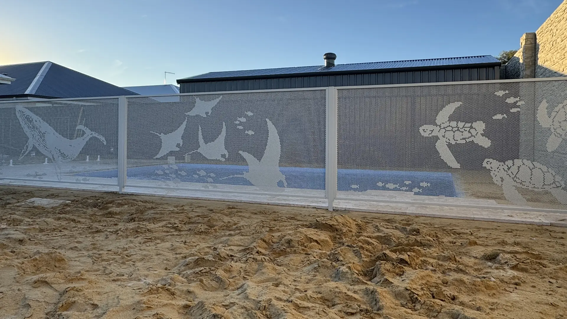 A white pool fence with whales, turtles and manta rays cut into it, the pool visible through it
