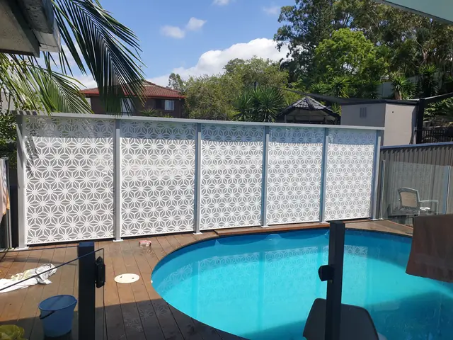 A white custom-design pool fence behind a round in-ground pool and timber deck