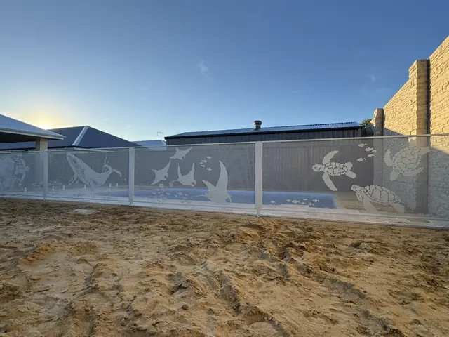 A white pool fence with whales, turtles and manta rays cut into it, the pool visible through it