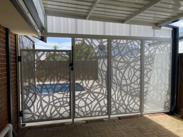 A white patterned pool gate and fence under a patio, the pool visible through it