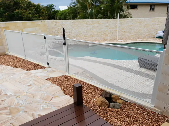 A pale Pure Perf pool fence around a freeform pool with sandstone paving
