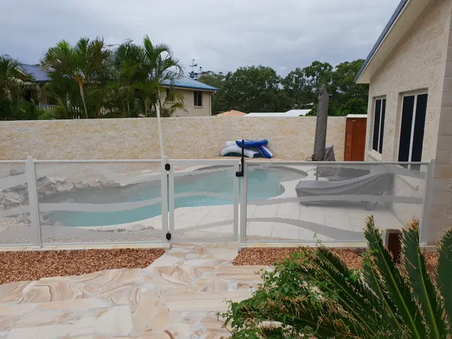 A pale pool fence and gate around a freeform pool beside a sandstone house