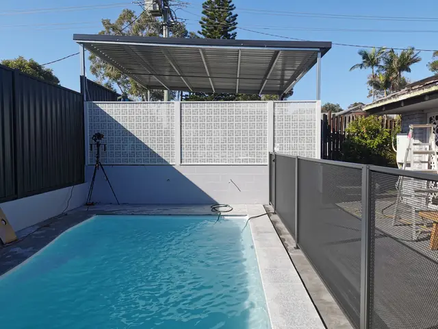 A white Nahosh design screen at the end of a lap pool, with a grey Pure Perf fence alongside