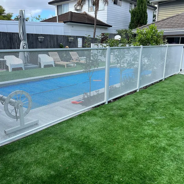 A white Pure Perf pool fence beside a pool with artificial turf and sun lounges