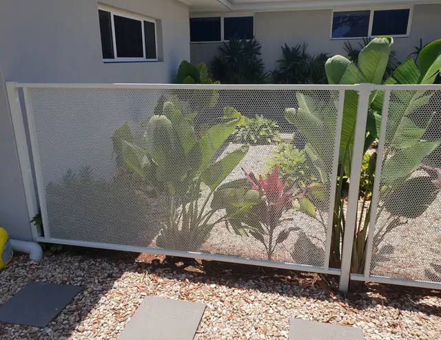 A white Pure Perf fence in front of a garden bed of palms and cordylines