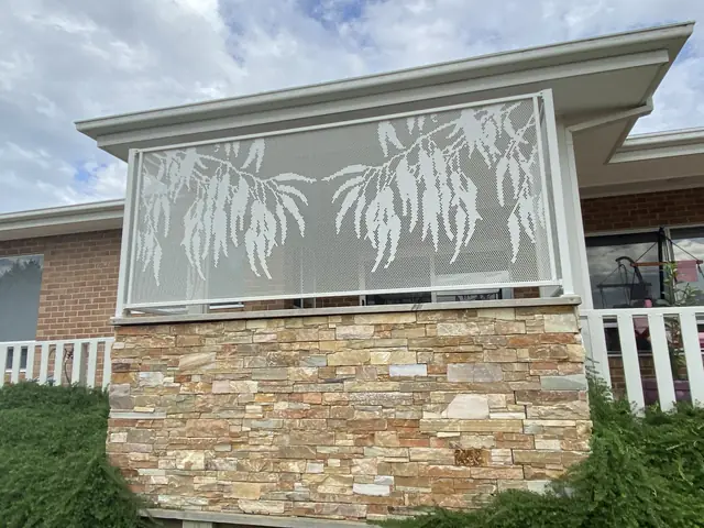 A white Gum design panel on a stone wall, with a white picket fence beside it
